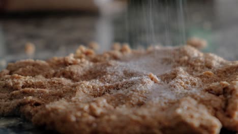 Dolly-out-close-up-of-woman-sprinkling-sugar-over-whole-wheat-dough-on-countertop