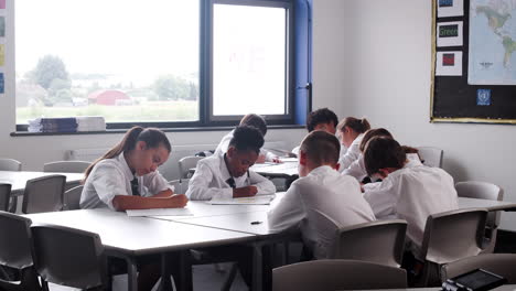 Gruppe-Von-Gymnasiasten-In-Uniform,-Die-An-Schreibtischen-Im-Klassenzimmer-Arbeiten