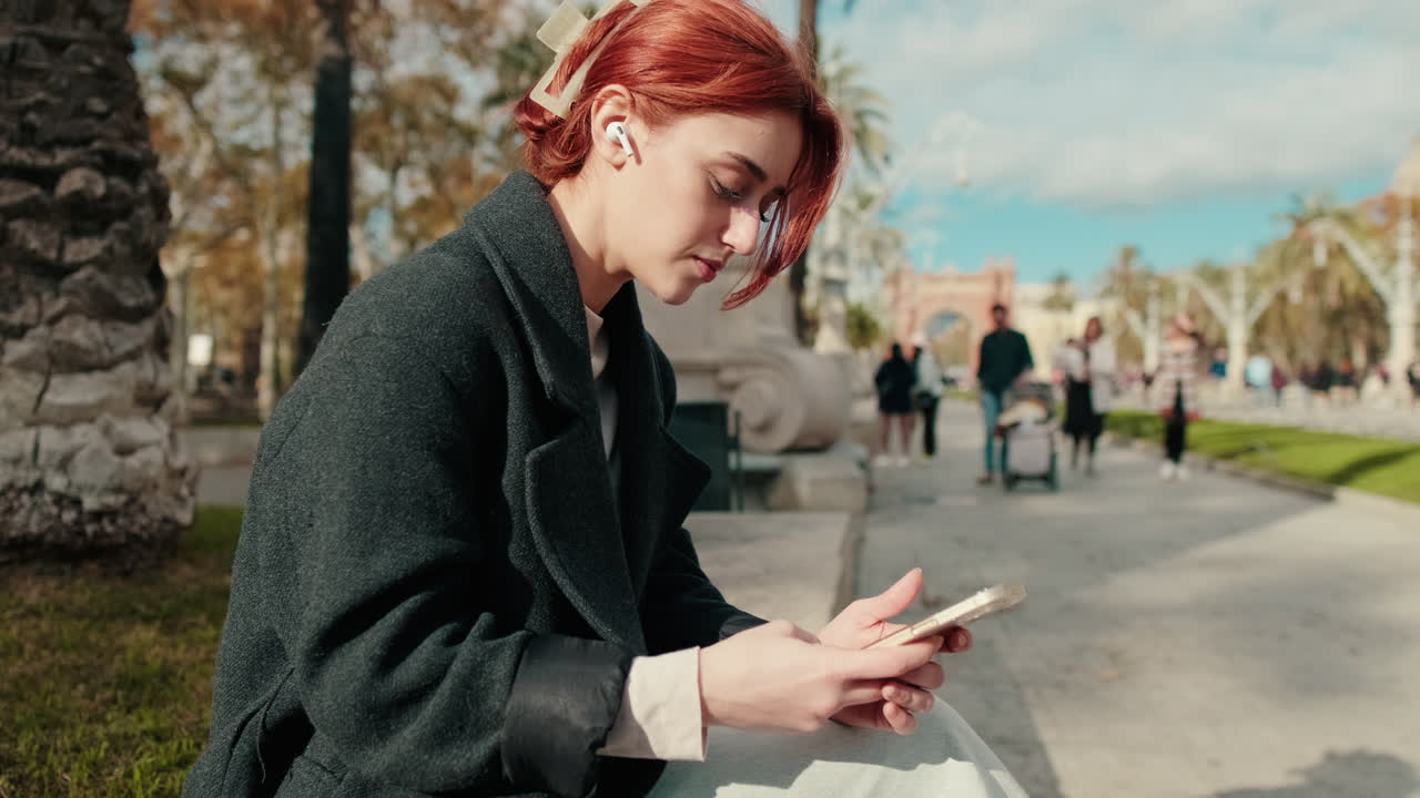 Young Redhead Woman Using Smartphone with Earbuds in Park