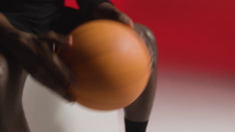 close up studio shot of seated male basketball player throwing ball from hand to hand against red background