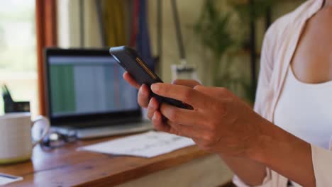 Mid-section-of-woman-using-smartphone-while-working-from-home