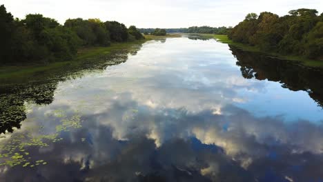 flying over a calm river, as the surface as a mirror reflecting the blue sky with clouds