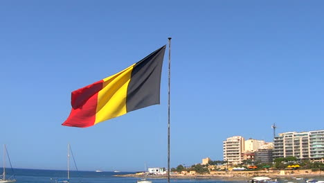 a german flag waving in slow motion on a bright sunny day with the sea, the maltese city and the blue sky in the backround.