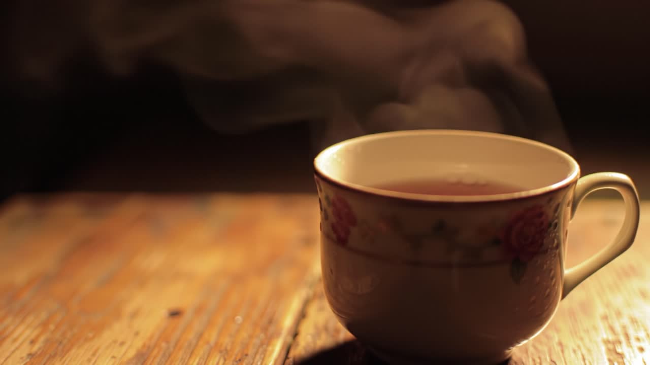 A delicate cup filled with warm tea stands on a rustic wooden surface. Soft steam rises in the evening light, creating a calm and cozy atmosphere perfect for relaxation.
