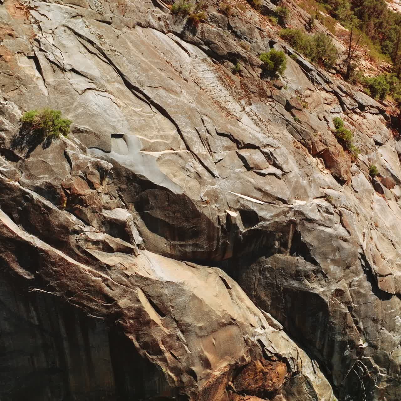 Close look at the bare grey rocks on sunny day. Huge cliff with rare greenery growing on the cliffs from top view