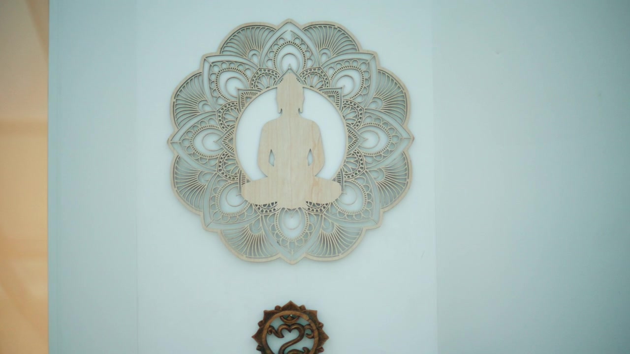 Silhouette di Buddha in legno che medita con uno sfondo di mandala spirituale su una parete chiara, simboleggiando pace, zen e consapevolezza.