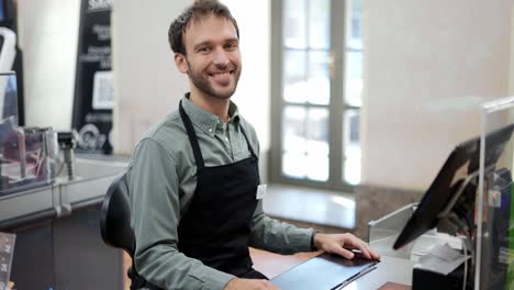 Handsome-man-in-supermarket-waiting-at-cash-desk-for-next-customer.-Smiling-cashier