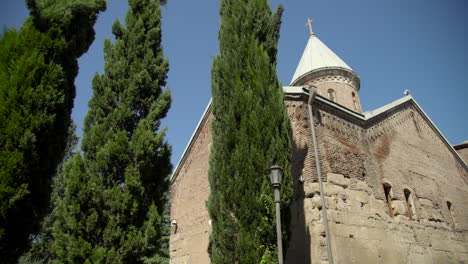 a low angle view over the trees of the 12th-century georgian orthodox church in the lurji monastery, or "blue church", in tbilisi georgia