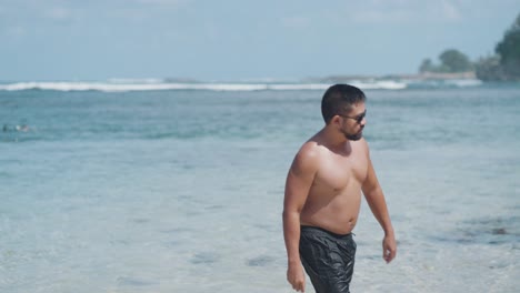 man walking in shallow ocean water at a beach