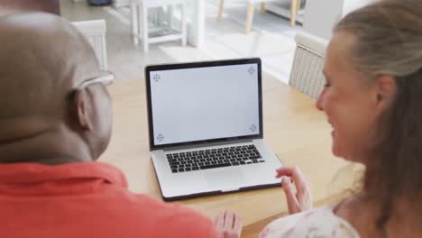 feliz pareja diversa mayor con camisas y usando computadora portátil con espacio de copia en la sala de estar