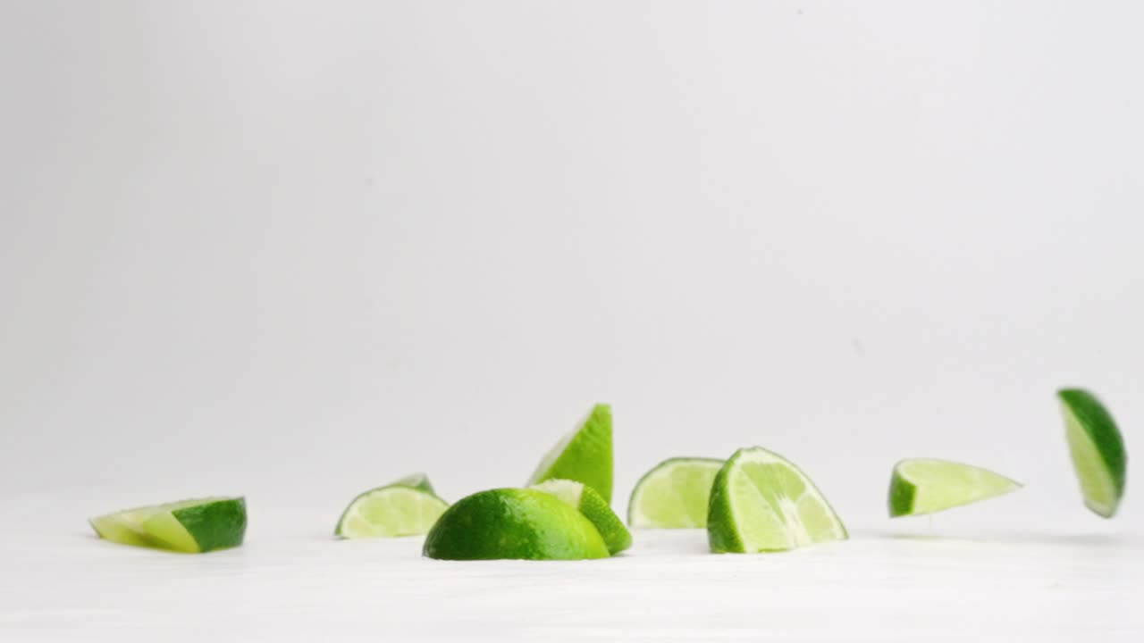 jugosas cuñas de lima verde rebotando en la parte superior de la mesa blanca en cámara lenta