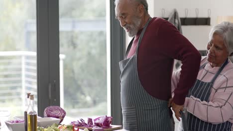 Senior-biracial-couple-wearing-aprons-in-kitchen,-unaltered,-in-slow-motion