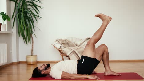 Sportsman-with-black-hair-exercises,-lifting-his-leg-up-in-the-living-room