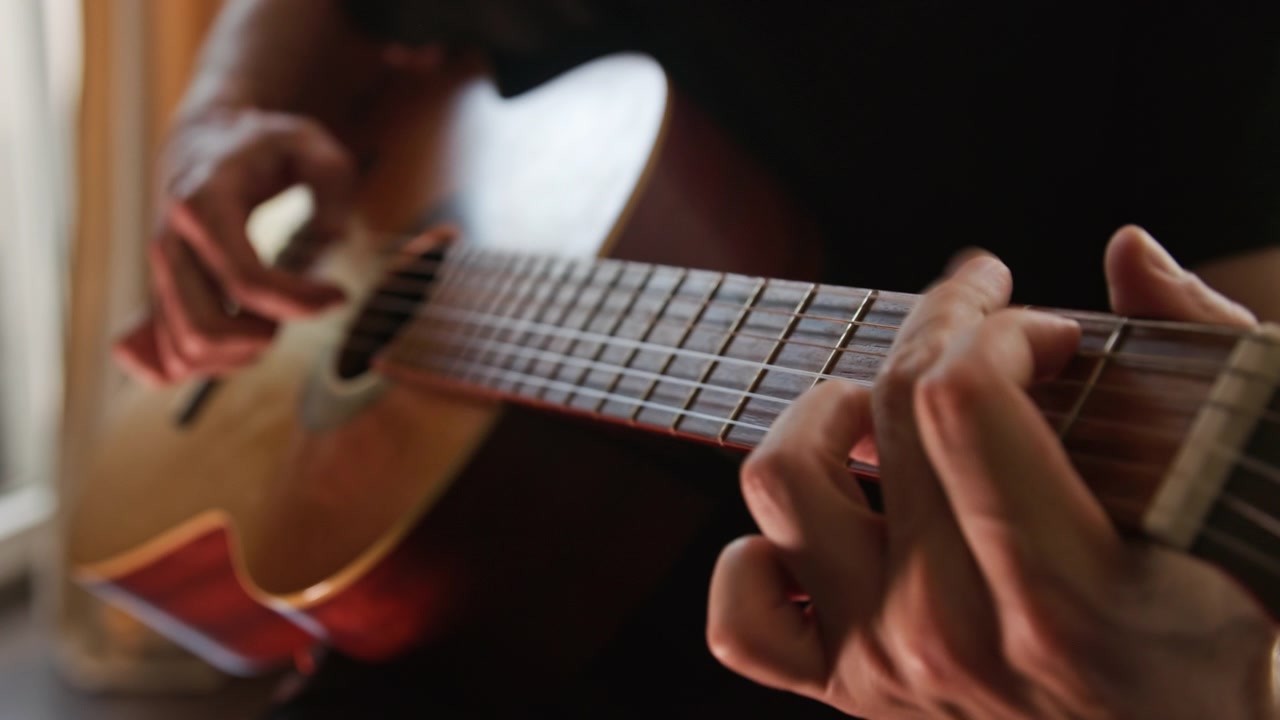 Un primo piano di una persona che suona una chitarra classica acustica al rallentatore, pizzicando gli accordi con le dita. Il video presenta una splendida illuminazione realistica e calda e un'ottima qualità estetica visiva