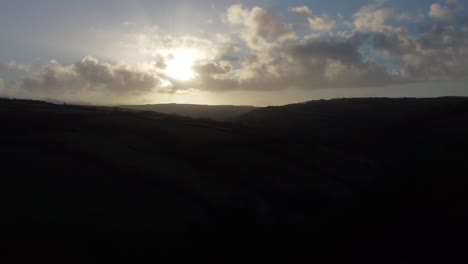 Descending-Aerial-View-of-Moorland-Landscape-at-Dawn-with-Sunrise-Behind-Dramatic-Cloudscape