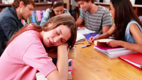 Studenten-Lernen-Zusammen-In-Der-Bibliothek-Mit-Mädchen,-Das-Auf-Büchern-Schläft