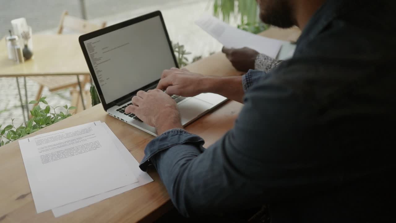 hombre escribiendo en una computadora portátil en una cafetería