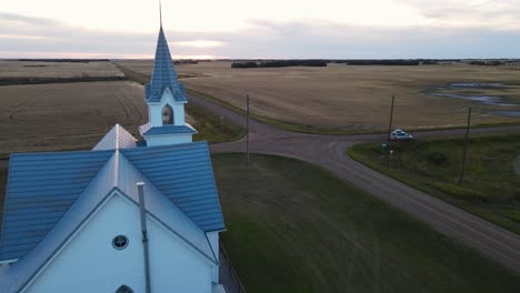 an ancient christian church made from wood behind a small patch of deciduous trees in rural alberta