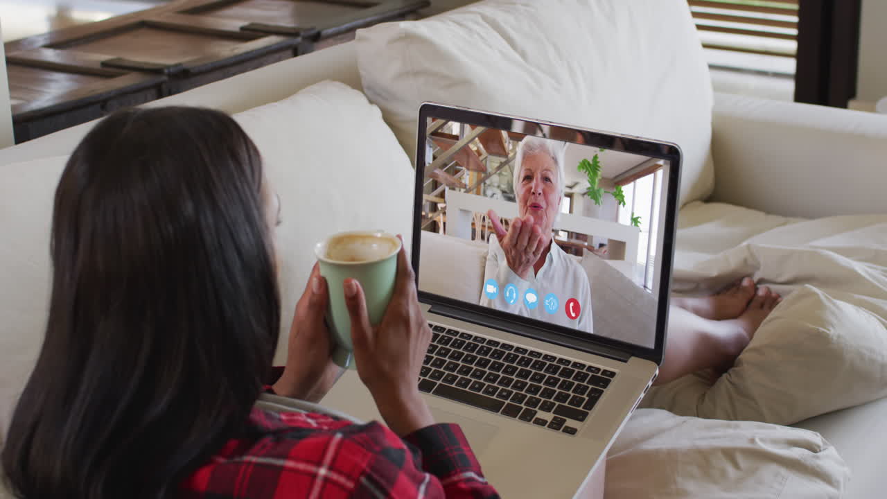 Biracial woman on laptop video chat having coffee at home
