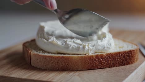 Close-up video of a hand spreading cream cheese on bread. The side angle captures the smooth texture
