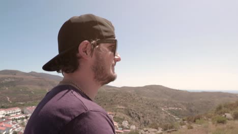 man with baseball hat and sunglasses walking around hills on sunny summer day