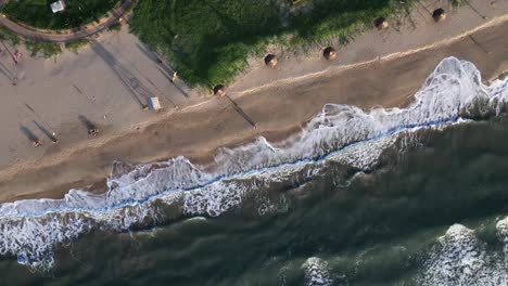 Aerial-birds-eye-descending-over-beach-with-unrecognizable-people-walking