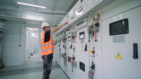 el ingeniero eléctrico que trabaja comprueba la tensión de corriente eléctrica y la sobrecarga en la parte delantera del gabinete del centro de carga o de la unidad de consumo para el mantenimiento en la sala principal del sistema de distribución de energía.