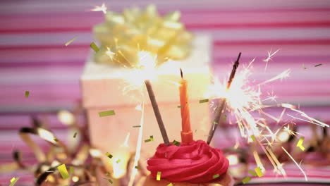 animation of gold confetti over hand holding match lighting candle and sparklers on birthday cupcake