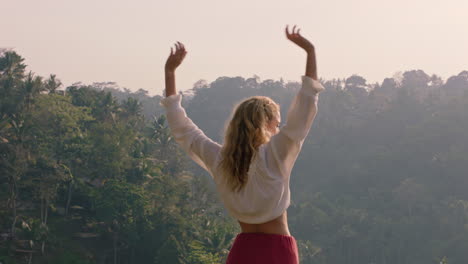 Mujer-Viajera-Celebrando-Con-Los-Brazos-Levantados-Mirando-La-Jungla-Tropical-Al-Amanecer-Sintiendo-Alegría-En-La-Aventura-De-Las-Vacaciones-De-Verano-Disfrutando-De-Un-Nuevo-Día-En-El-Paraíso