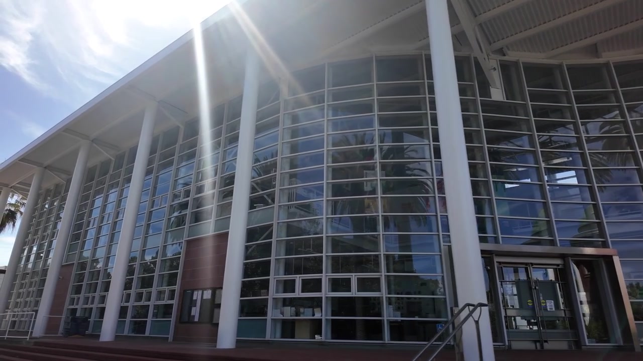 Vista esterna soleggiata della moderna facciata in vetro dell'Emeryville Civic Center in California, che mostra il suo design architettonico contemporaneo con colonne bianche e un grande ingresso
