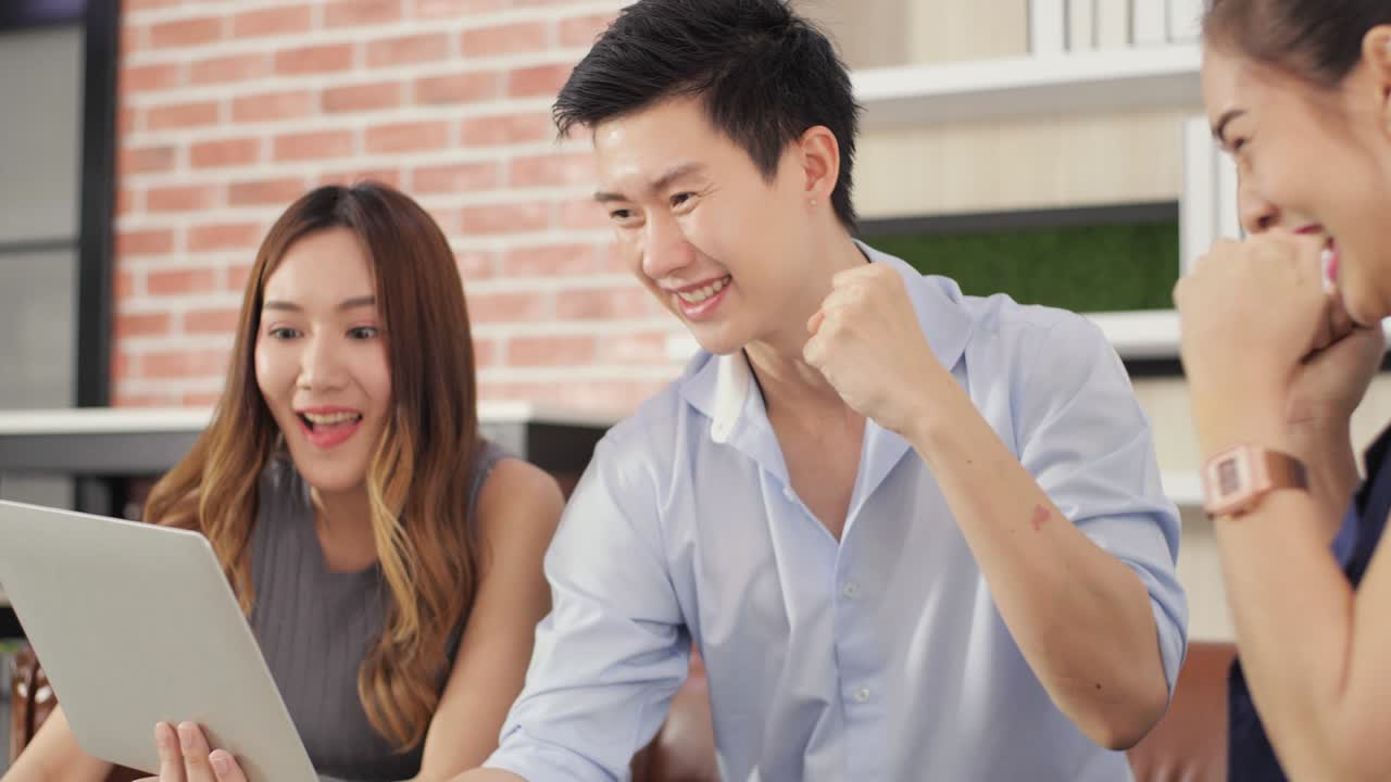 Asian business team celebrate success look at laptop in coffee restaurant