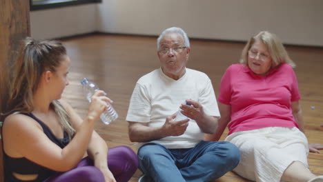 senior people sitting on floor in ballroom with dance teacher