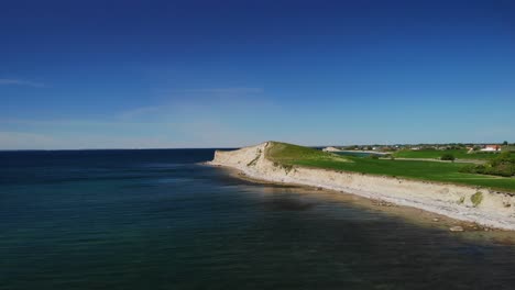 aerial 4k of danish coastline on a beautiful summer day with lush green fields and a small cliff down to the calm blue ocean