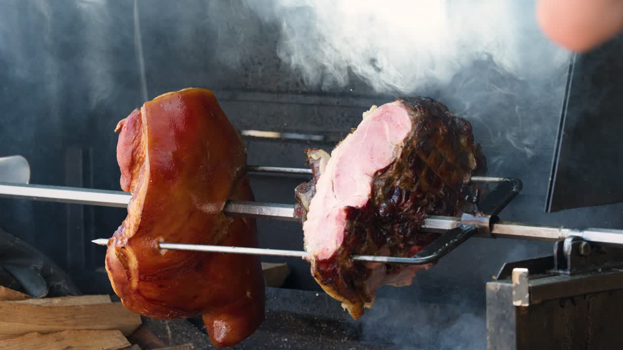 Cook rotates smoked pork ham over open flame, smoky outdoor market, natural daylight, close-up view