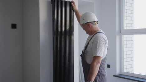 a man plumber in a helmet checks modern batteries for heat output and heating system. heating season