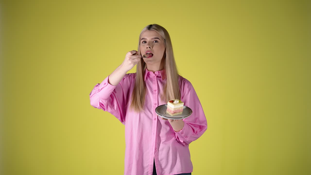Young Blonde Woman Holding Plate Of Cake and Eating With Fork, Studio Portrait