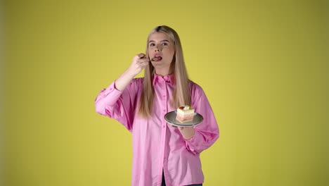 young blonde woman holding plate of cake and eating with fork, studio portrait