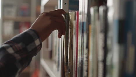 man hand picks up book from shelf in library closeup. african american reader seeks literature to prepare for exams in information center. reading hobby