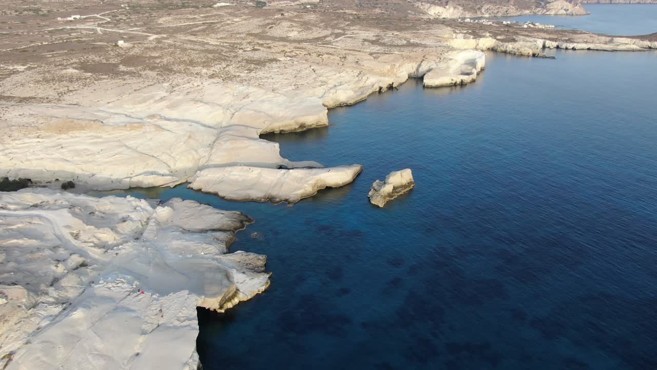 Drone view in Greece flying over a moon shaped white rock area in Milos island at sunrise next to the dark blue sea