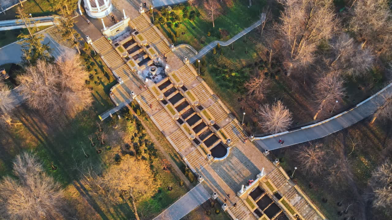 Aerial drone view of Chisinau cascade staircase at sunset. Multiple bare trees, walking people. Moldova