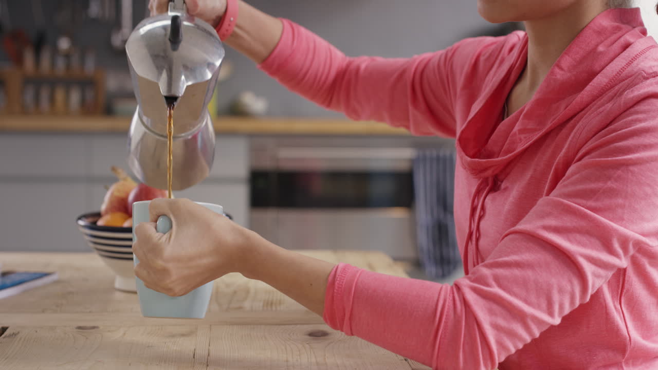 hermosa mujer de raza mixta vertiendo café por la mañana en la cocina en casa