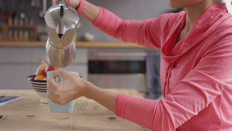 hermosa mujer de raza mixta vertiendo café por la mañana en la cocina en casa