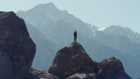 Young-hiker-standing-on-rocky-boulder-with-view-of-Sierra-Nevada-range,-aerial