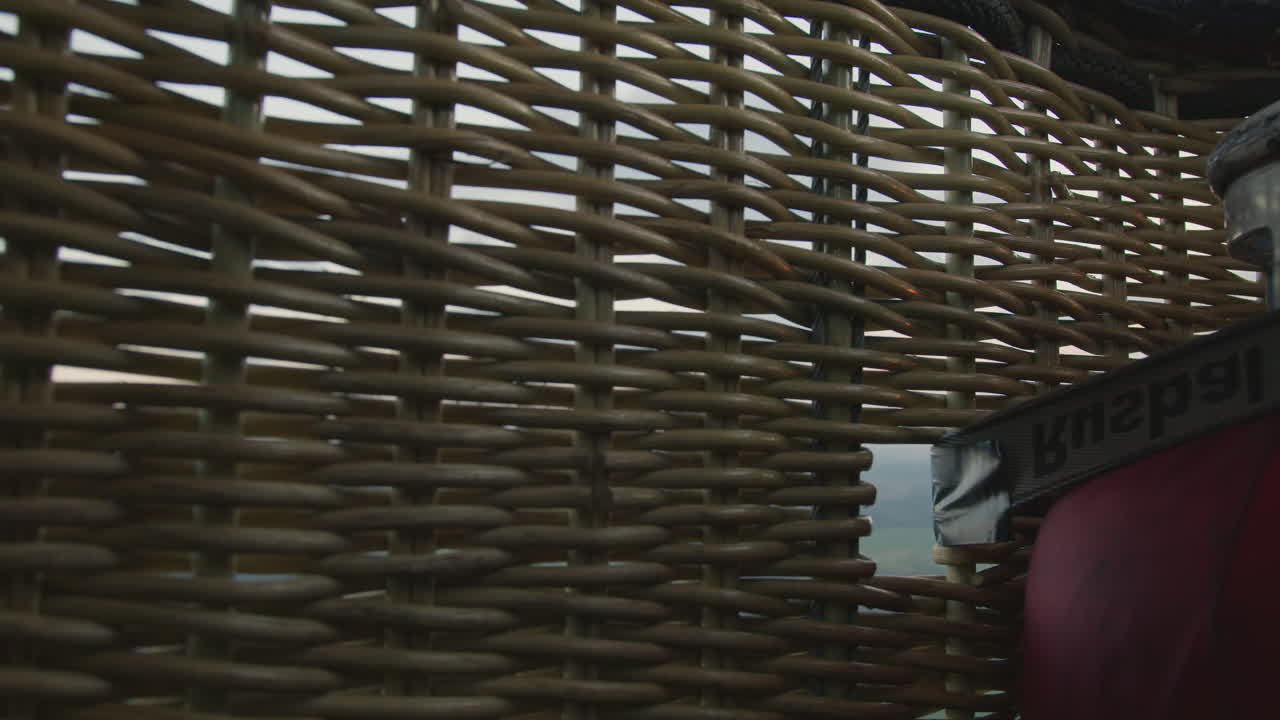 Close up of woven basket side from hot air balloon gently floating above patchwork fields at sunset with soft sky tones and subtle horizon line conveying serene aerial perspective and tactile texture