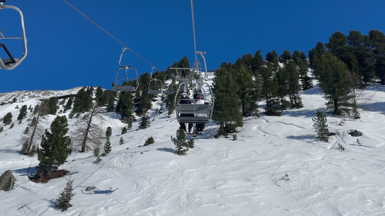 POV on 2-person chairlift up sunny mountain snow ski slope in trees