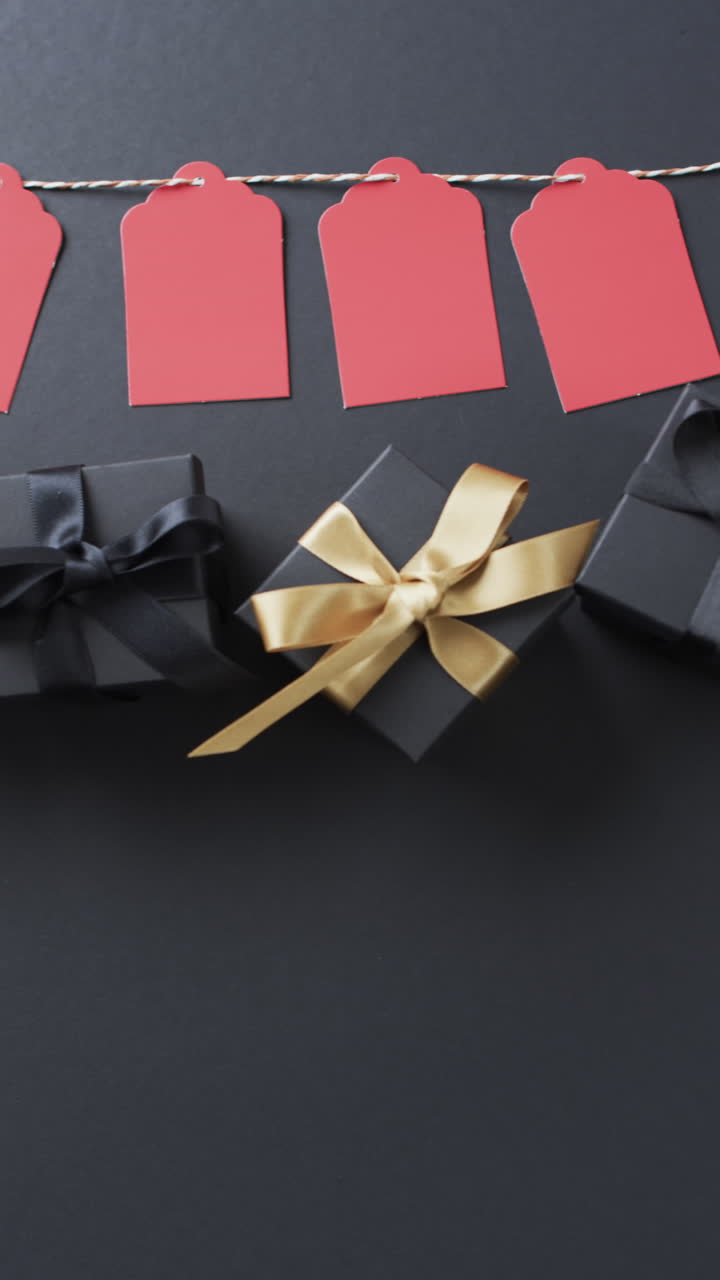 Vertical video of gift tags on string, gift boxes with ribbons and copy space on black background