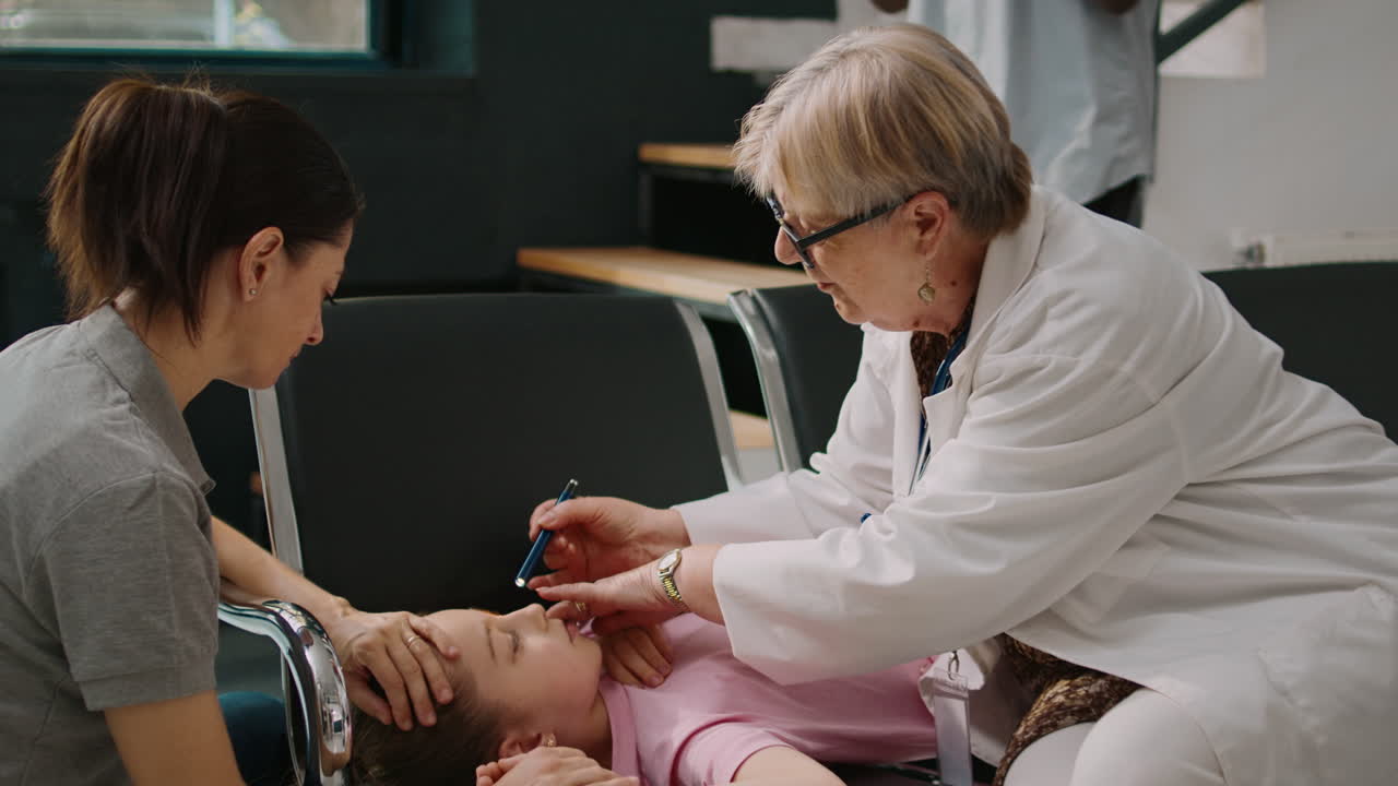 Elderly physician consulting small unconscious child with flashlight