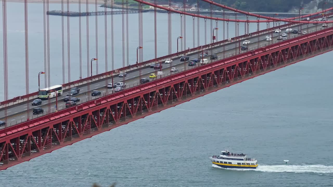 Steady shot of Golden Gate Bridge with traffic and ferry with surfer passing by