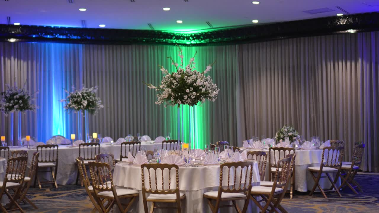sala de recepción de banquete de boda decorada con varias mesas blancas con piezas centrales altas