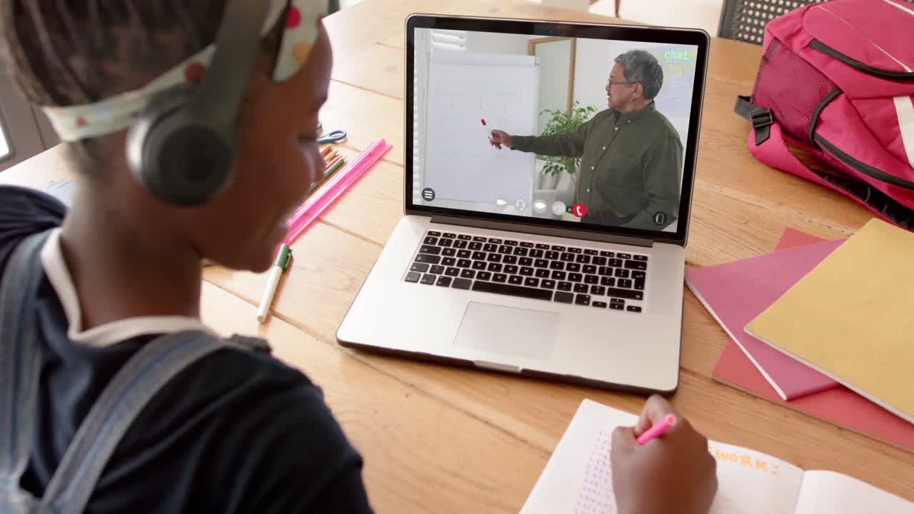 estudiante afroamericana usando una computadora portátil para una lección en línea con un profesor masculino biracial en la pantalla